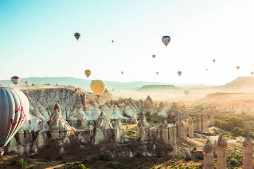 A stunning aerial view of hot air balloons floating over Cappadocia's rocky terrain during a sunny day.