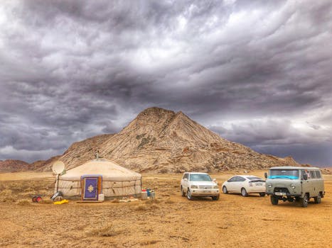 Scenic view of a Mongolian yurt and vehicles in Bayan-Unjuul with dramatic skies.